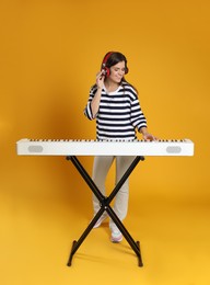 Photo of Smiling woman in headphones playing synthesizer on orange background