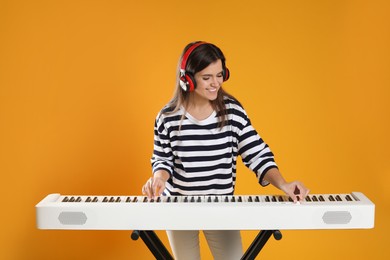 Photo of Smiling woman in headphones playing synthesizer on orange background