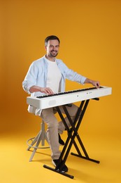 Photo of Smiling man playing synthesizer on orange background