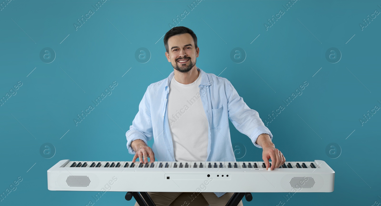 Photo of Smiling man playing synthesizer on light blue background