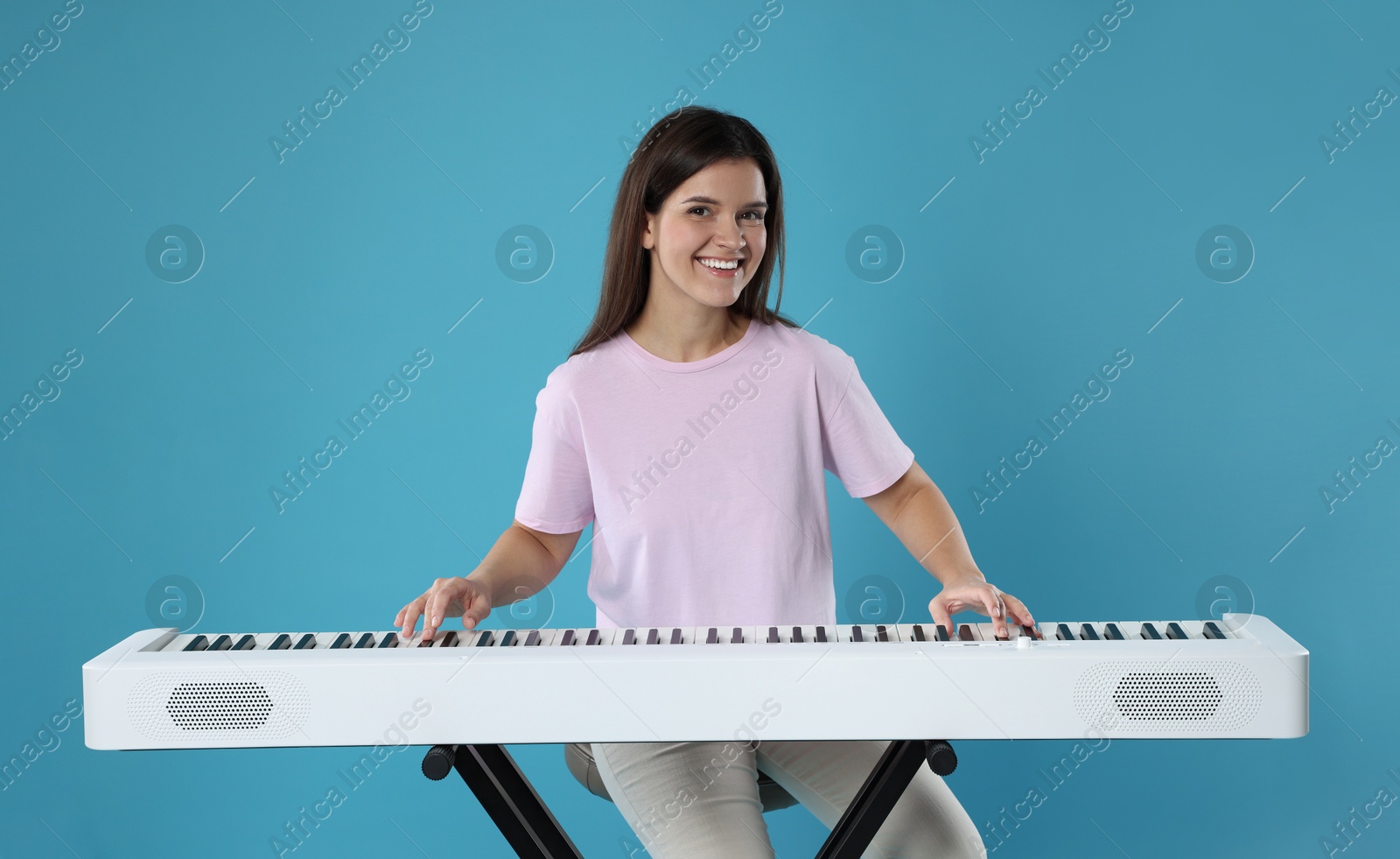 Photo of Smiling woman playing synthesizer on light blue background