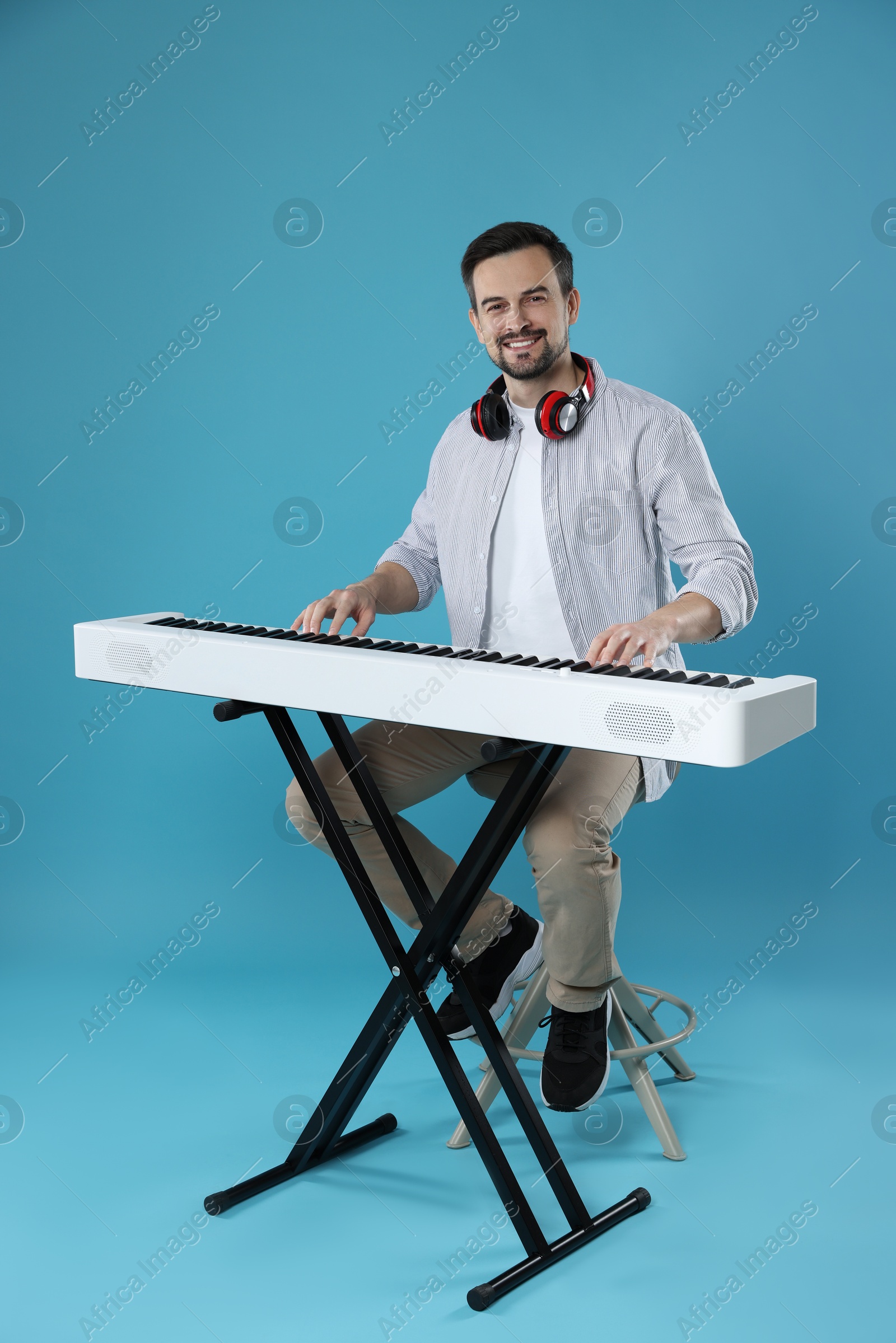 Photo of Smiling man playing synthesizer on light blue background