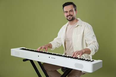 Photo of Smiling man playing synthesizer on olive background