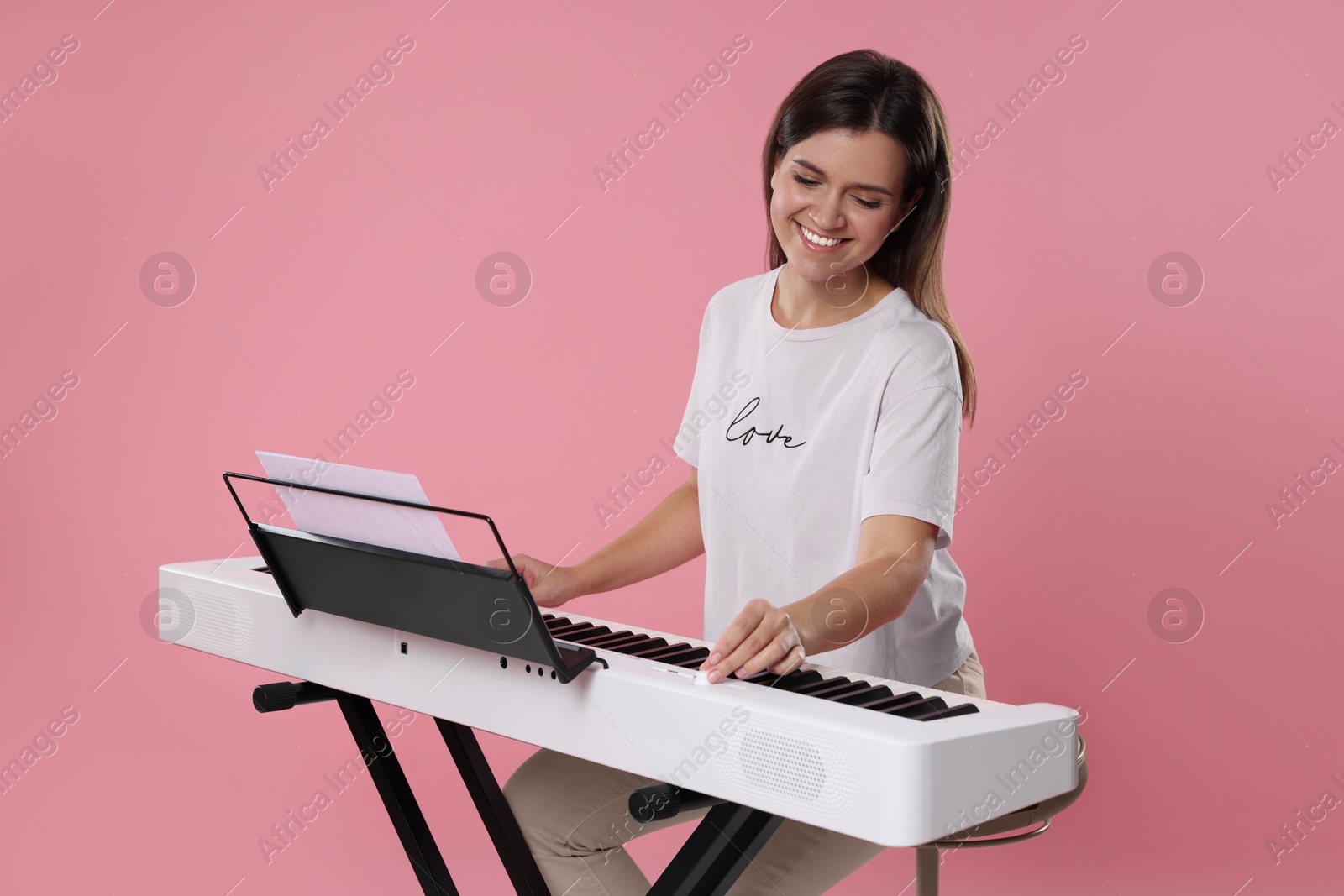 Photo of Smiling woman playing synthesizer on pink background