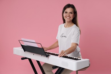 Photo of Smiling woman playing synthesizer on pink background