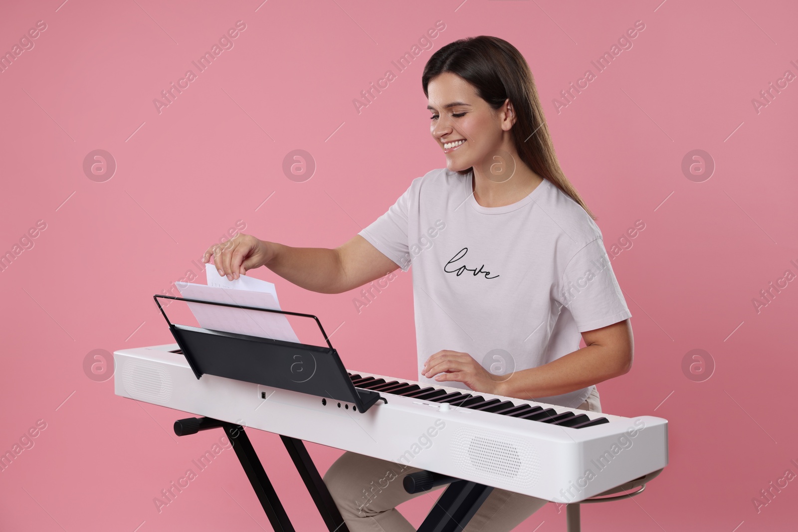 Photo of Smiling woman playing synthesizer on pink background