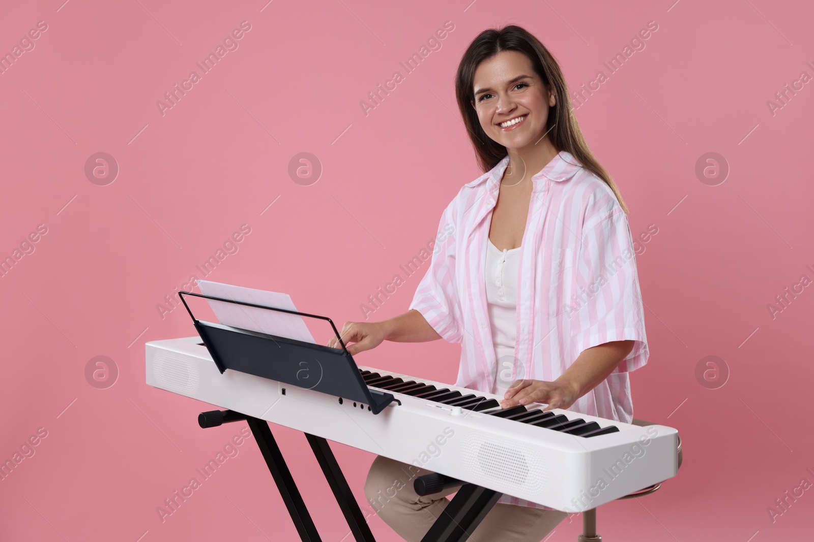 Photo of Smiling woman playing synthesizer on pink background