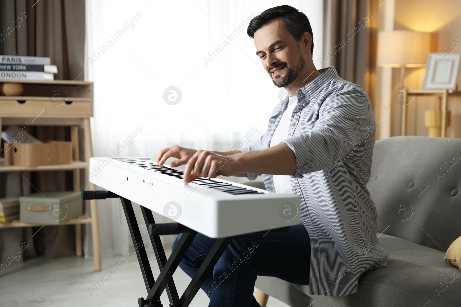 Photo of Smiling man playing synthesizer at home. Electronic musical instrument