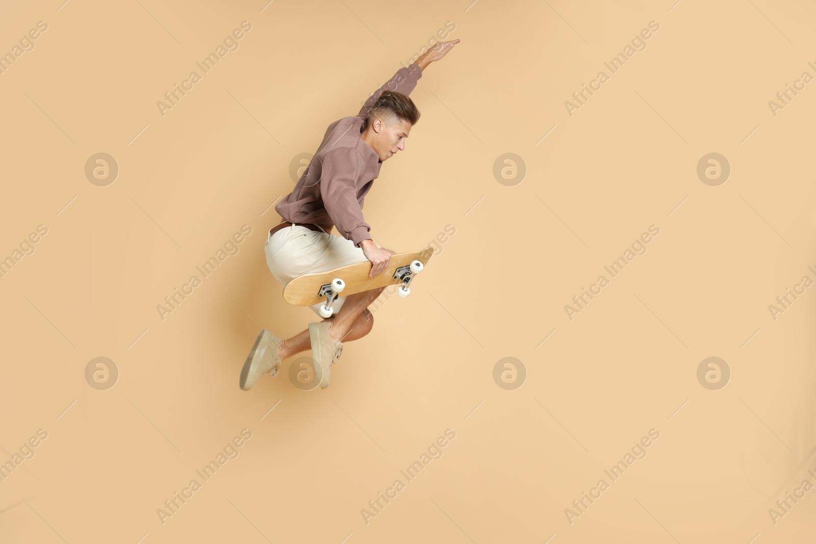 Photo of Handsome man jumping with skateboard on beige background. Space for text