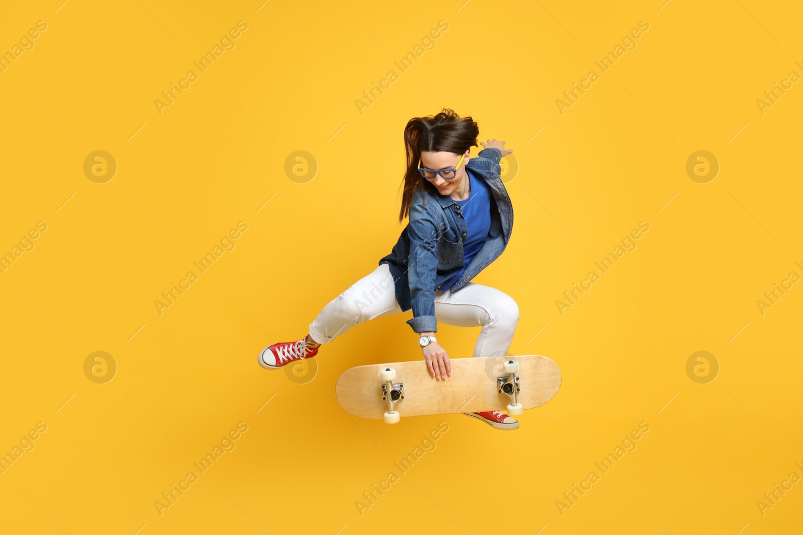 Photo of Smiling woman jumping with skateboard on orange background