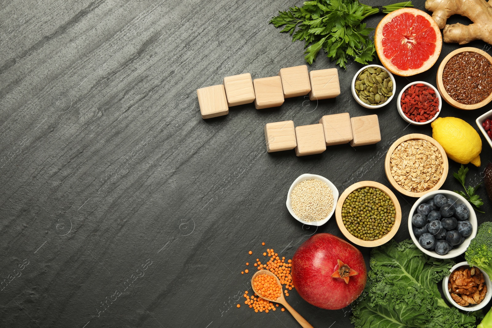 Photo of Superfood. Different healthy food products and blank wooden cubes on grey table, flat lay. Space for text