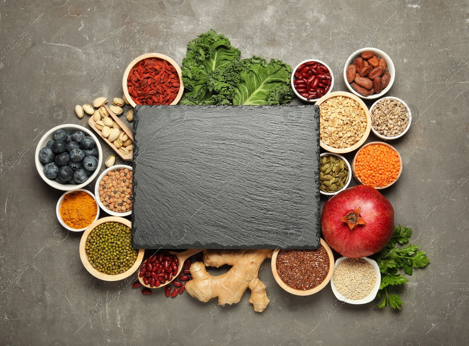 Photo of Superfood. Different healthy food products and blank board on grey table, flat lay. Space for text