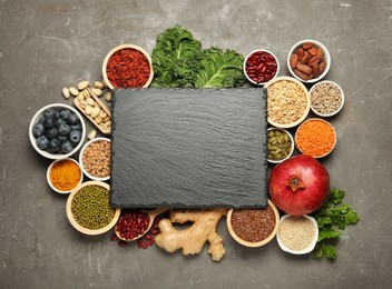 Photo of Superfood. Different healthy food products and blank board on grey table, flat lay. Space for text