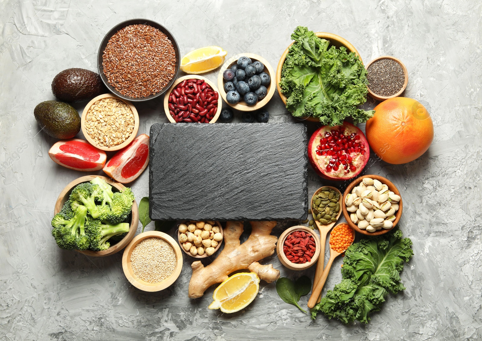 Photo of Different superfood products and blank slate board on grey table, flat lay. Space for text