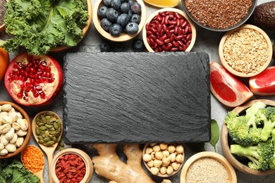 Photo of Different superfood products and blank slate board on grey table, flat lay. Space for text