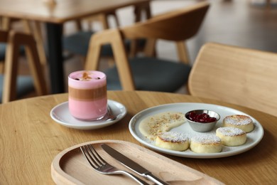 Photo of Delicious cottage cheese pancakes and pink latte served on wooden table indoors