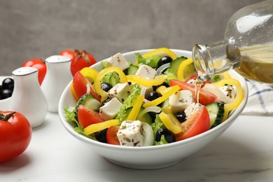 Photo of Adding olive oil to Greek salad at white marble table, closeup