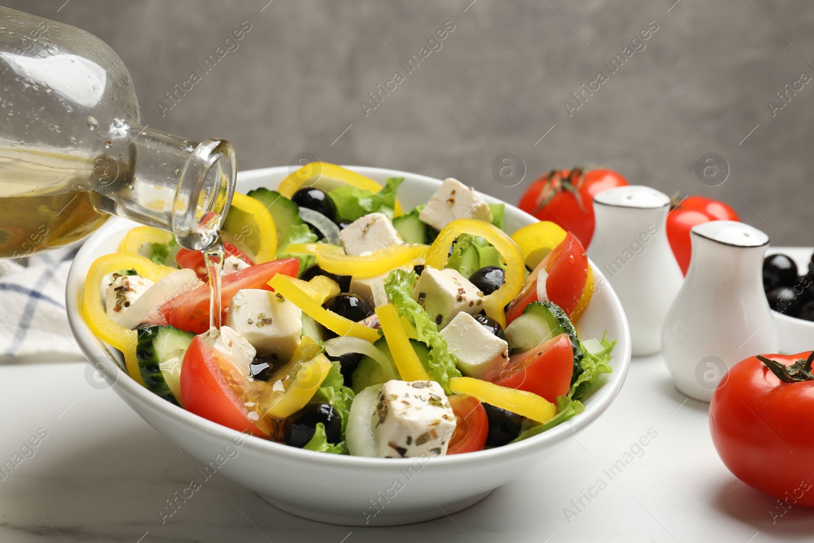 Photo of Adding olive oil to Greek salad at white marble table, closeup