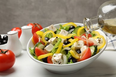 Photo of Adding olive oil to Greek salad at white marble table, closeup