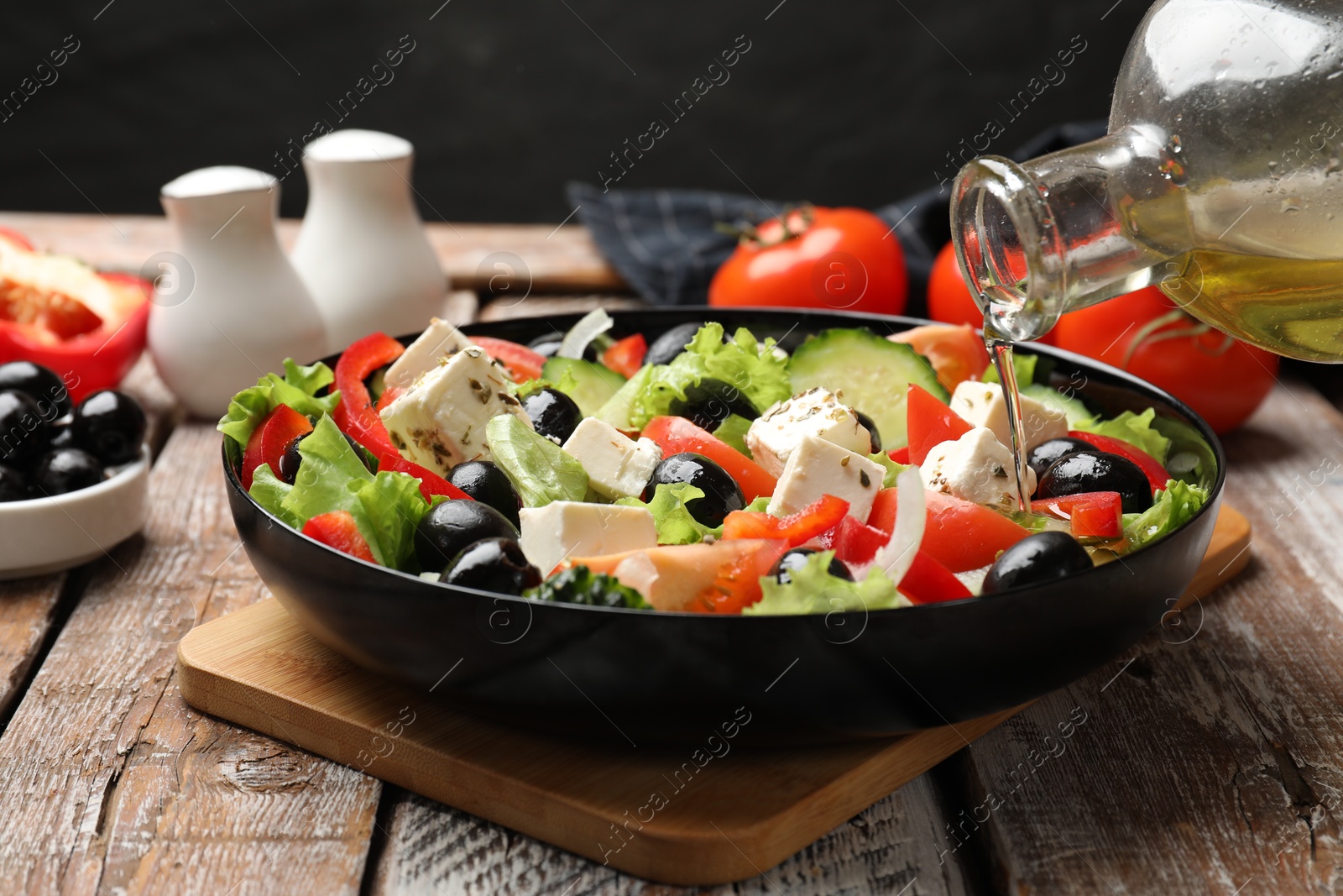 Photo of Adding olive oil to Greek salad at wooden table, closeup