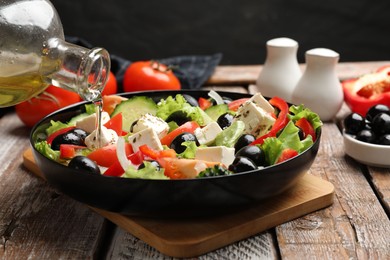 Photo of Adding olive oil to Greek salad at wooden table, closeup