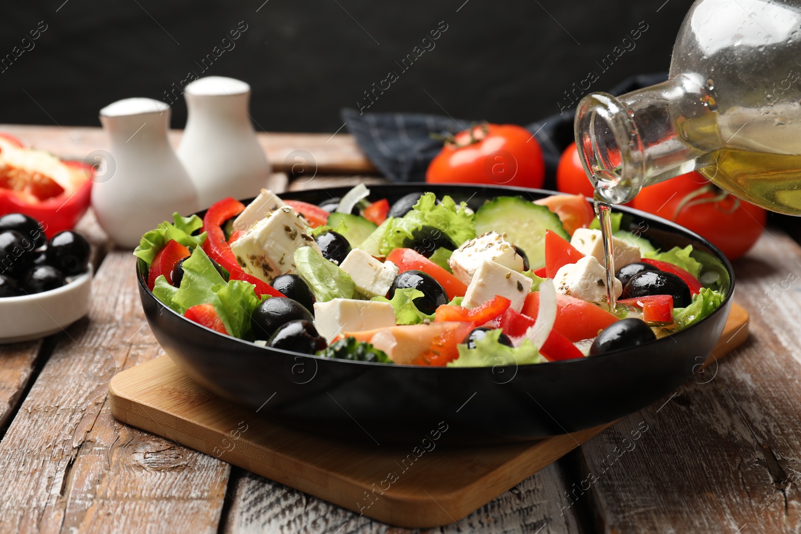 Photo of Adding olive oil to Greek salad at wooden table, closeup