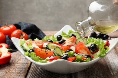 Photo of Adding olive oil to Greek salad at wooden table, closeup