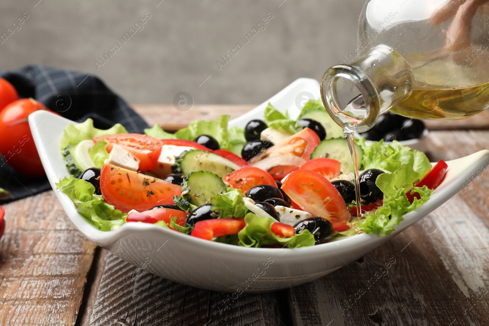 Photo of Adding olive oil to Greek salad at wooden table, closeup