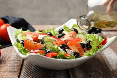 Photo of Adding olive oil to Greek salad at wooden table, closeup