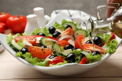 Photo of Adding olive oil to Greek salad at white wooden table, closeup