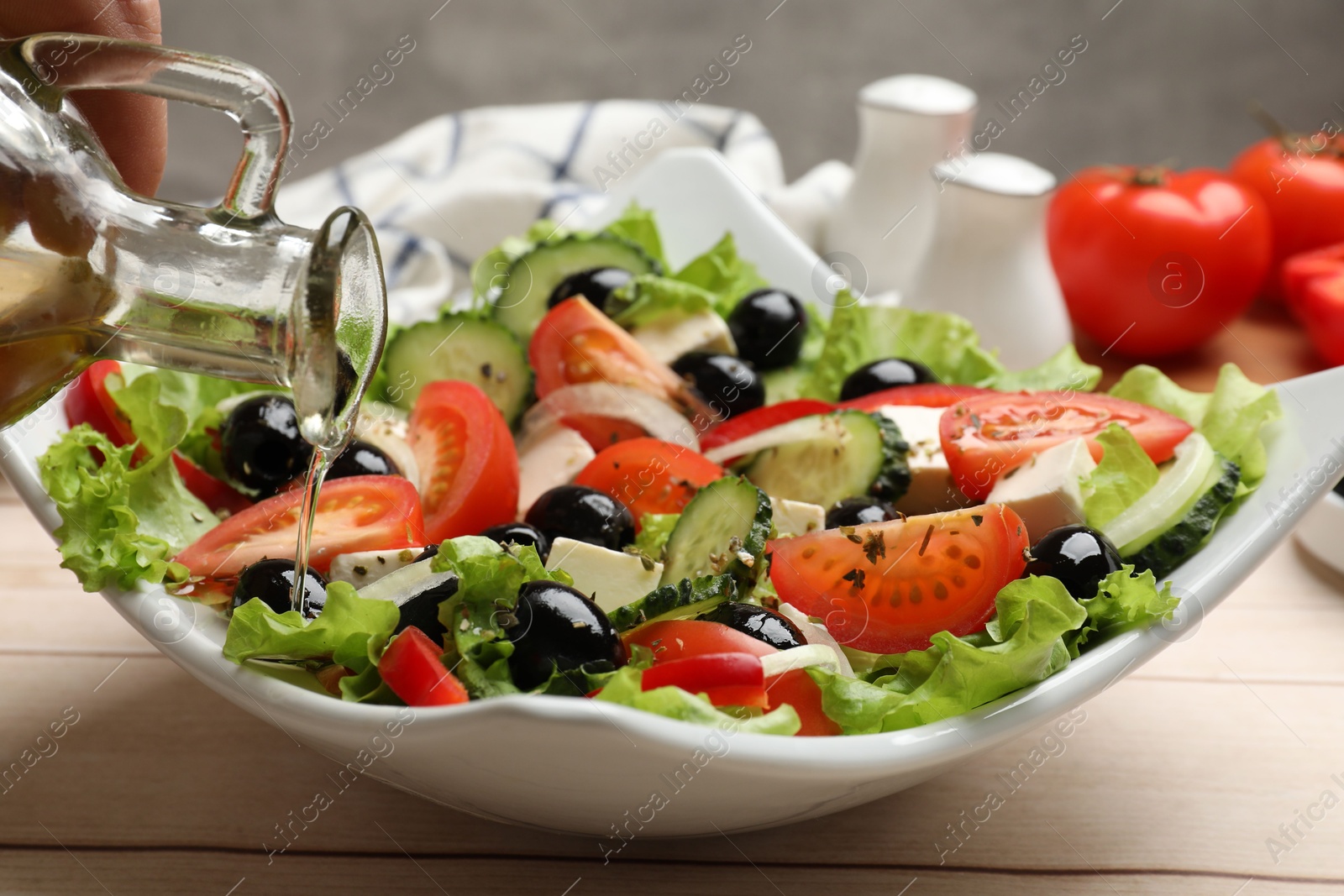 Photo of Adding olive oil to Greek salad at white wooden table, closeup