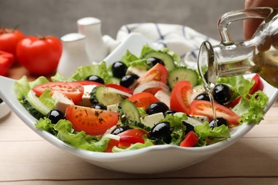 Photo of Adding olive oil to Greek salad at white wooden table, closeup