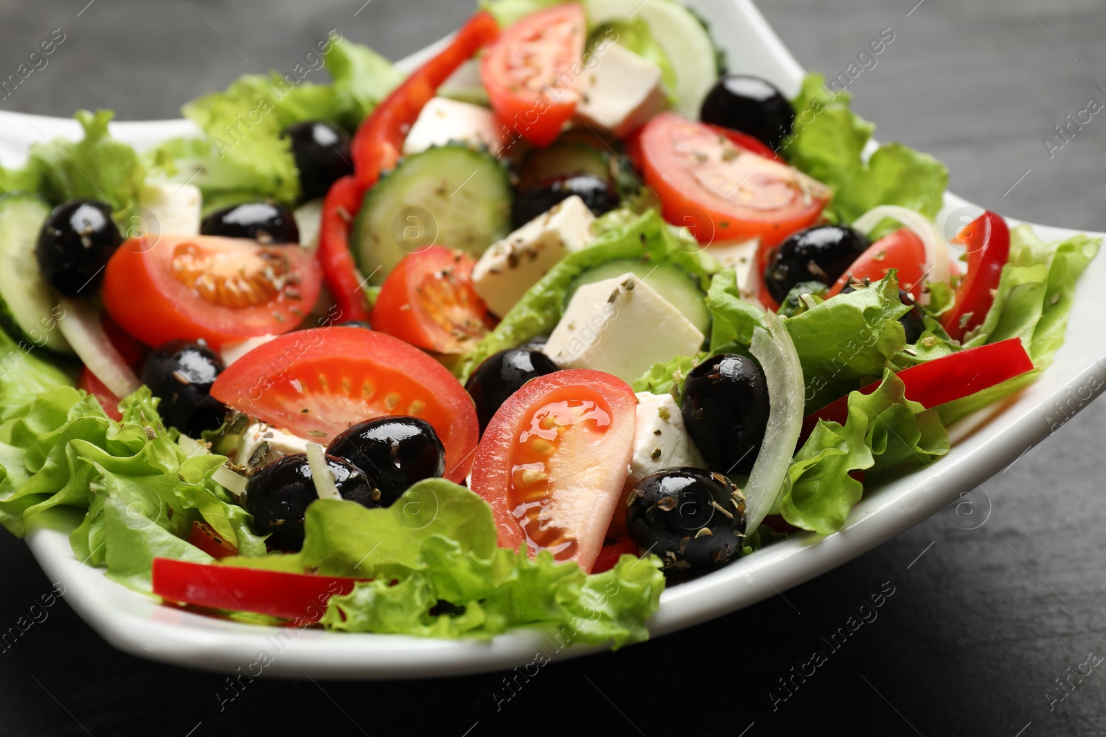 Photo of Delicious fresh Greek salad on black table, closeup