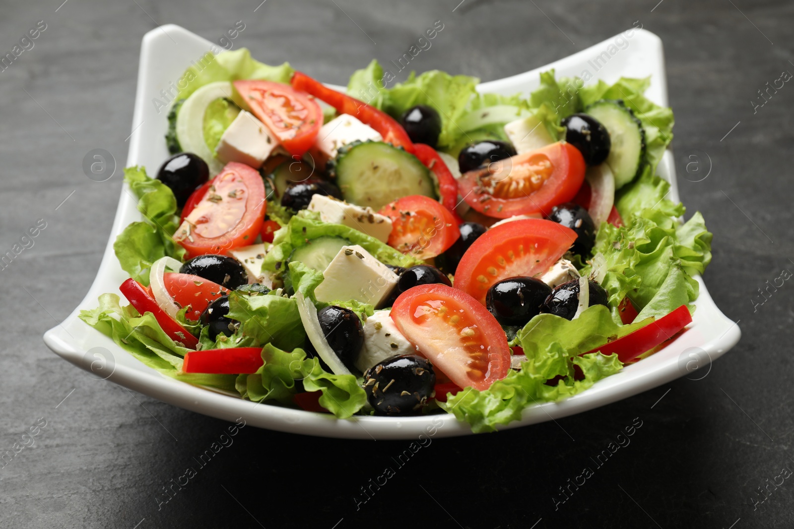 Photo of Delicious fresh Greek salad on black table, closeup