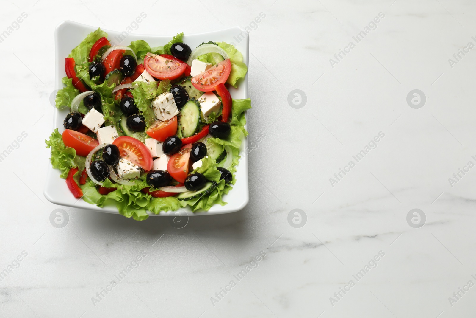 Photo of Delicious fresh Greek salad on white marble table, top view. Space for text