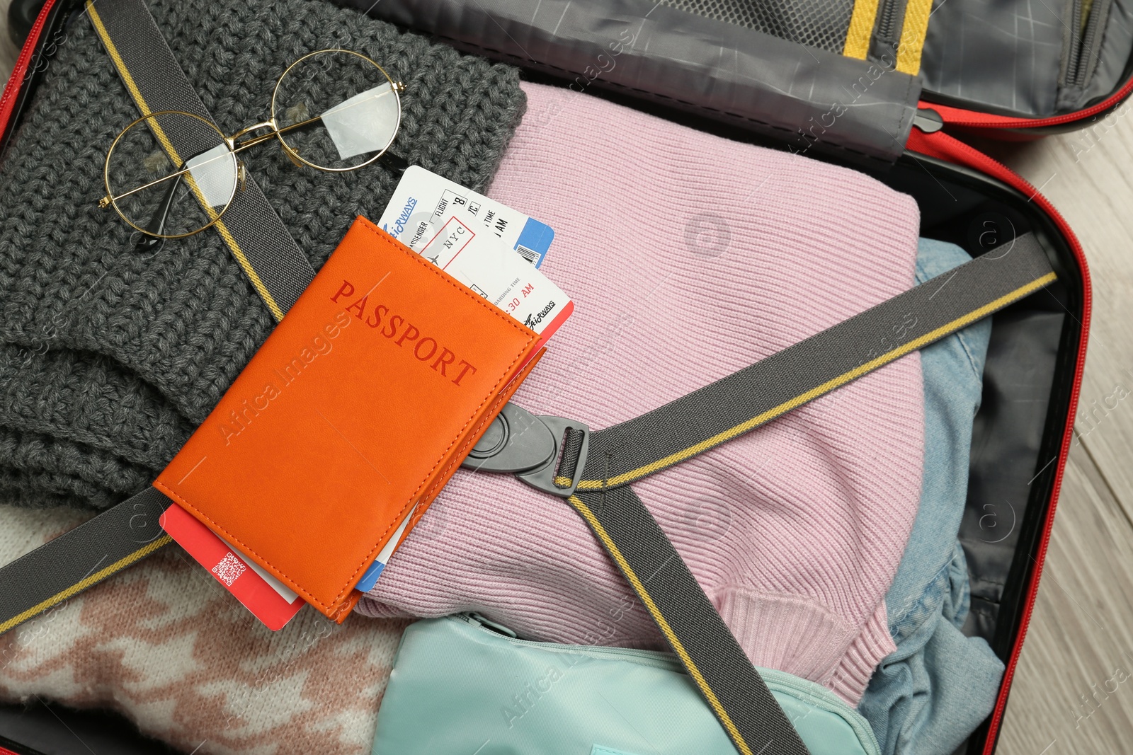 Photo of Passport with ticket and glasses on packed suitcase indoors, top view