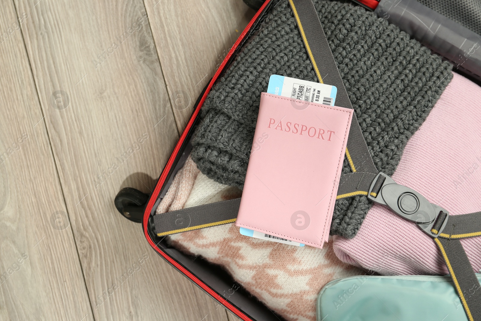 Photo of Passport with ticket on packed suitcase indoors, top view