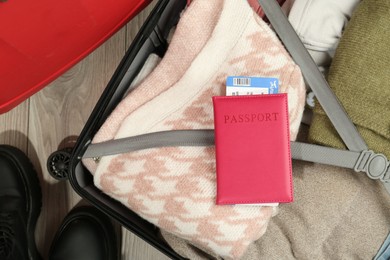 Photo of Passport with ticket on packed suitcase indoors, top view