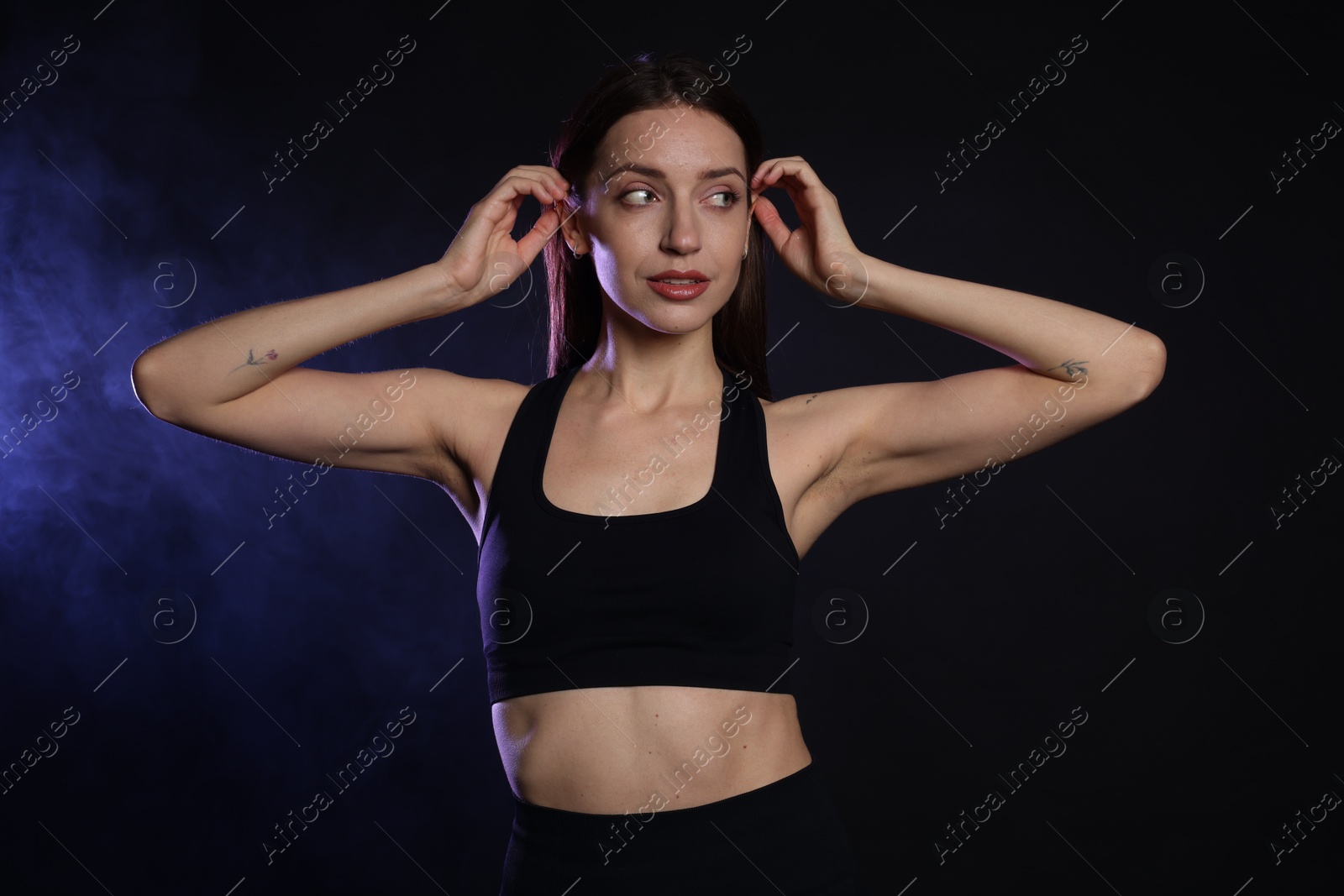 Photo of Beautiful woman in stylish sportswear on dark background with color light and smoke