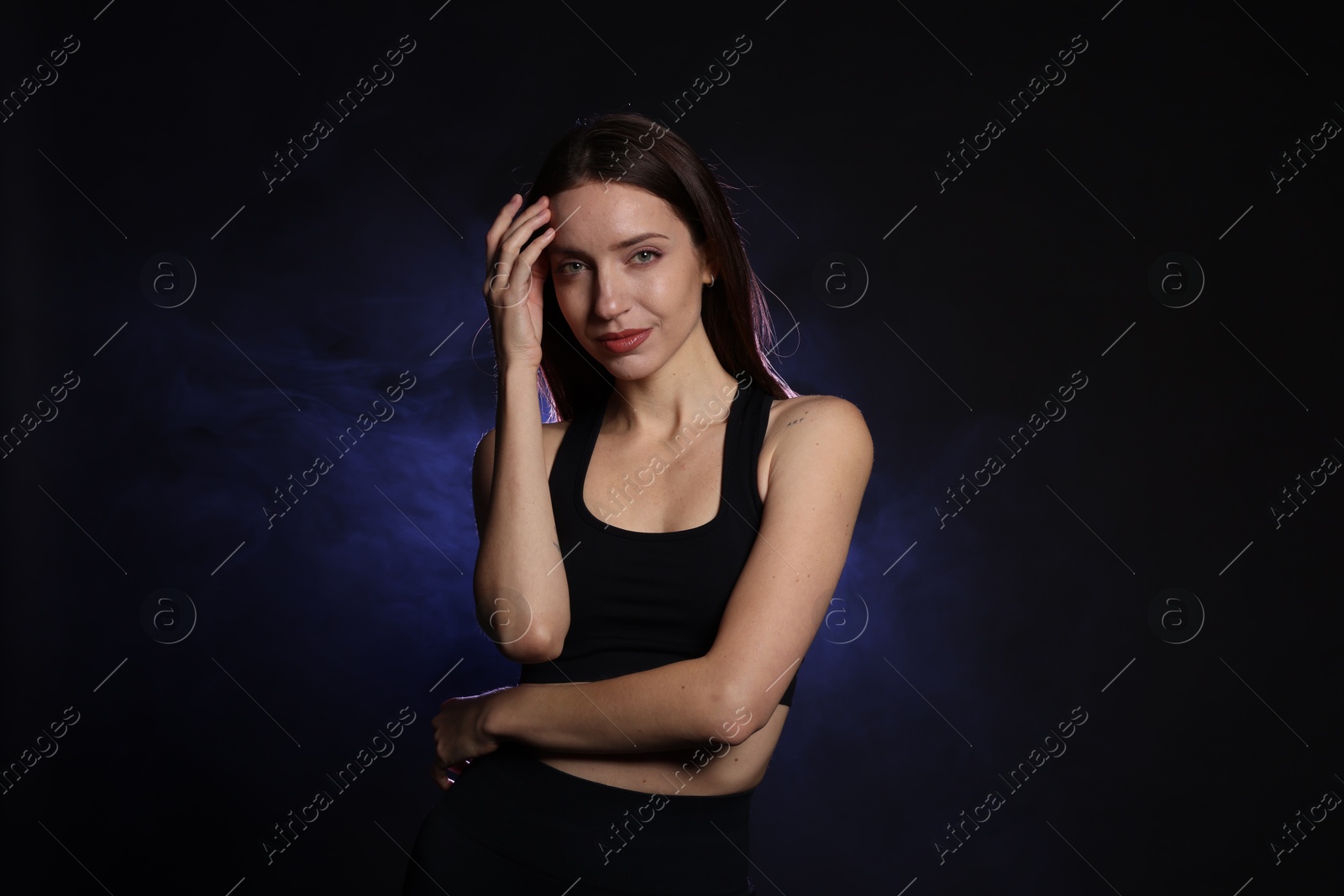 Photo of Beautiful woman in stylish sportswear on dark background with color light and smoke