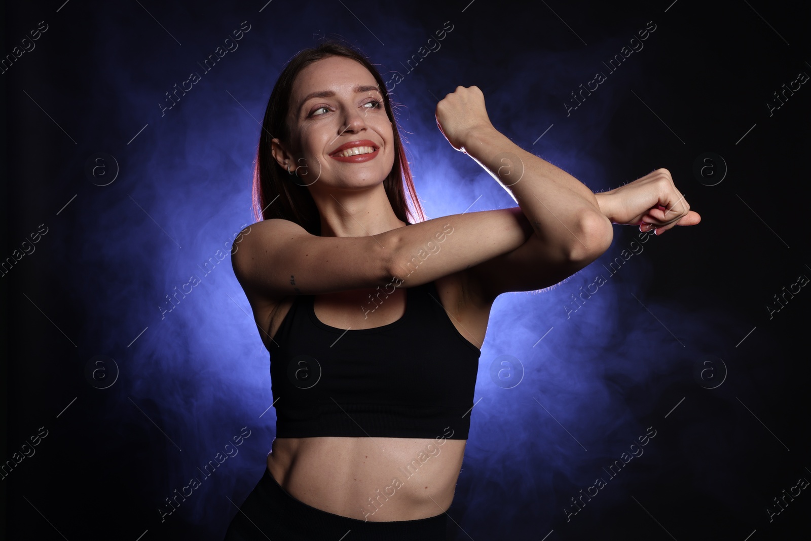 Photo of Beautiful woman in stylish sportswear on dark background with color light and smoke