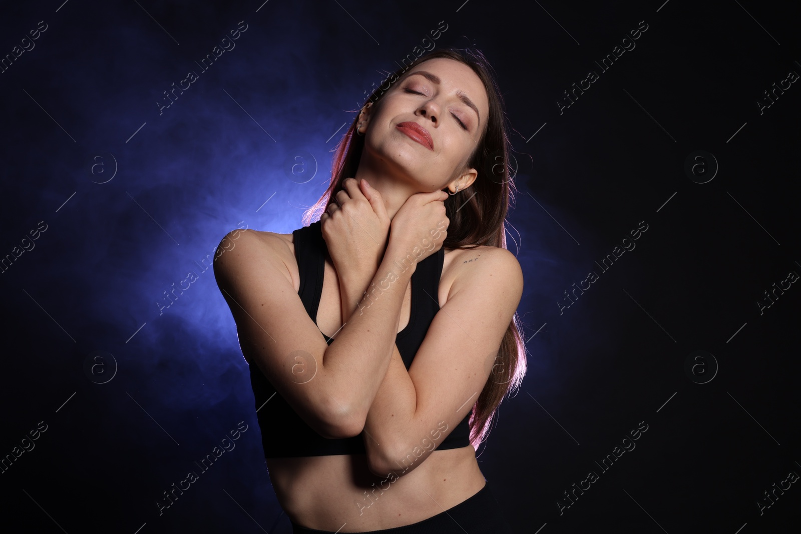 Photo of Beautiful woman in stylish sportswear on dark background with color light and smoke