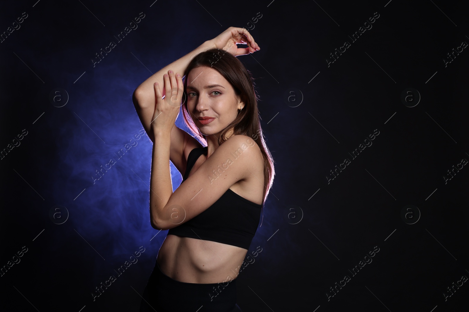 Photo of Beautiful woman in stylish sportswear on dark background with color light and smoke