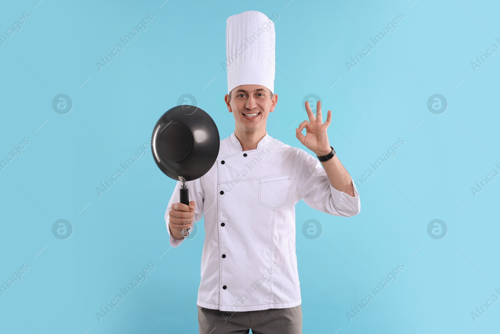 Photo of Professional chef with wok showing okay gesture on light blue background