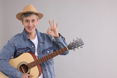 Photo of Happy man with guitar showing okay gesture on light grey background. Space for text