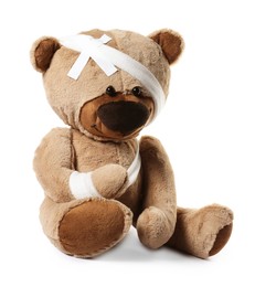 Photo of Teddy bear with bandages and adhesive medical plasters isolated on white