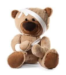 Photo of Teddy bear with bandages and adhesive medical plasters isolated on white