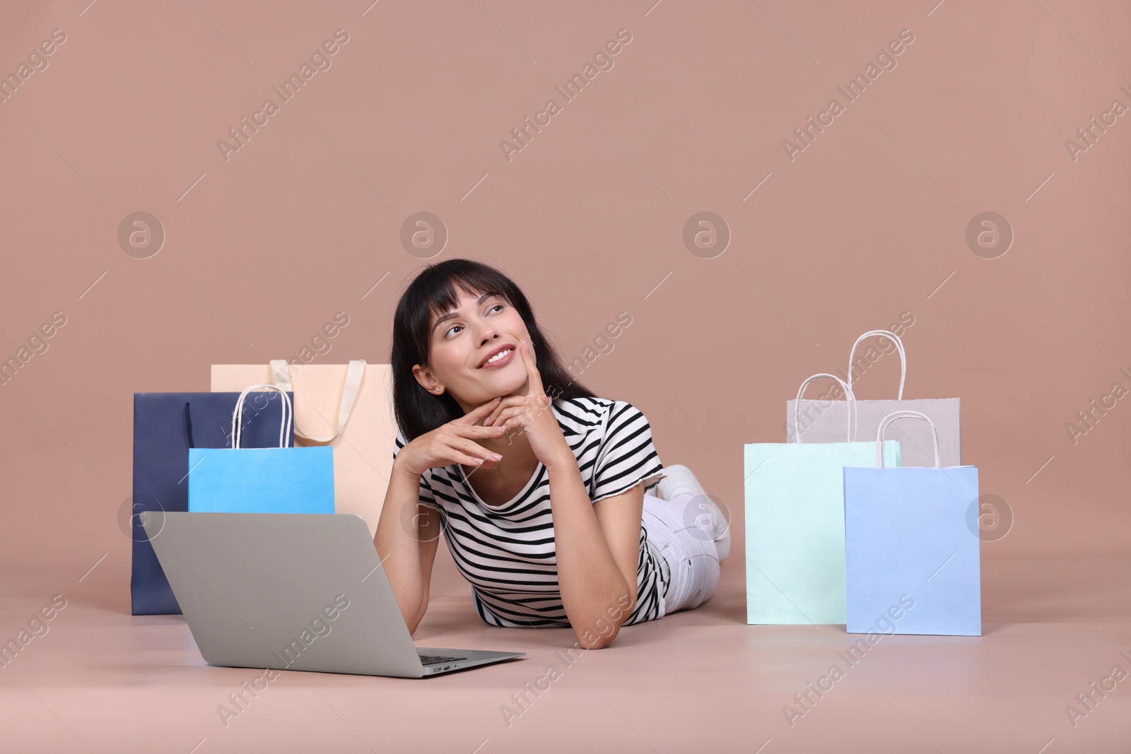 Photo of Internet shopping. Happy woman with laptop and colorful bags on beige background