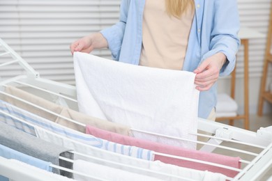 Photo of Woman hanging fresh clean laundry on drying rack at home, closeup