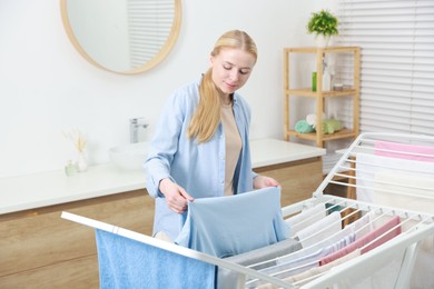 Photo of Beautiful woman hanging fresh clean laundry on drying rack at home